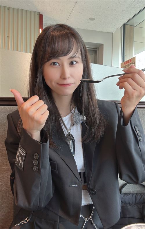 YouTuberあま猫が黒いスーツジャケットと白トップスでレストランで食事。ネックレスが輝くスタイリッシュな装いで、モダンなインテリアが背景の大人なライフスタイル。SNSで人気のグルメVlogシーン。