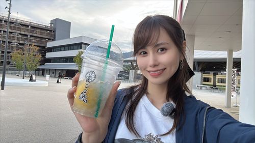 YouTuberあま猫が白いTシャツとパーカーで屋外ベンチに座り、スターバックスのアイスドリンクを手に笑顔のセルフィー。都市のビルが背景の爽やかな日常がSNSで人気のライフスタイルVlog。